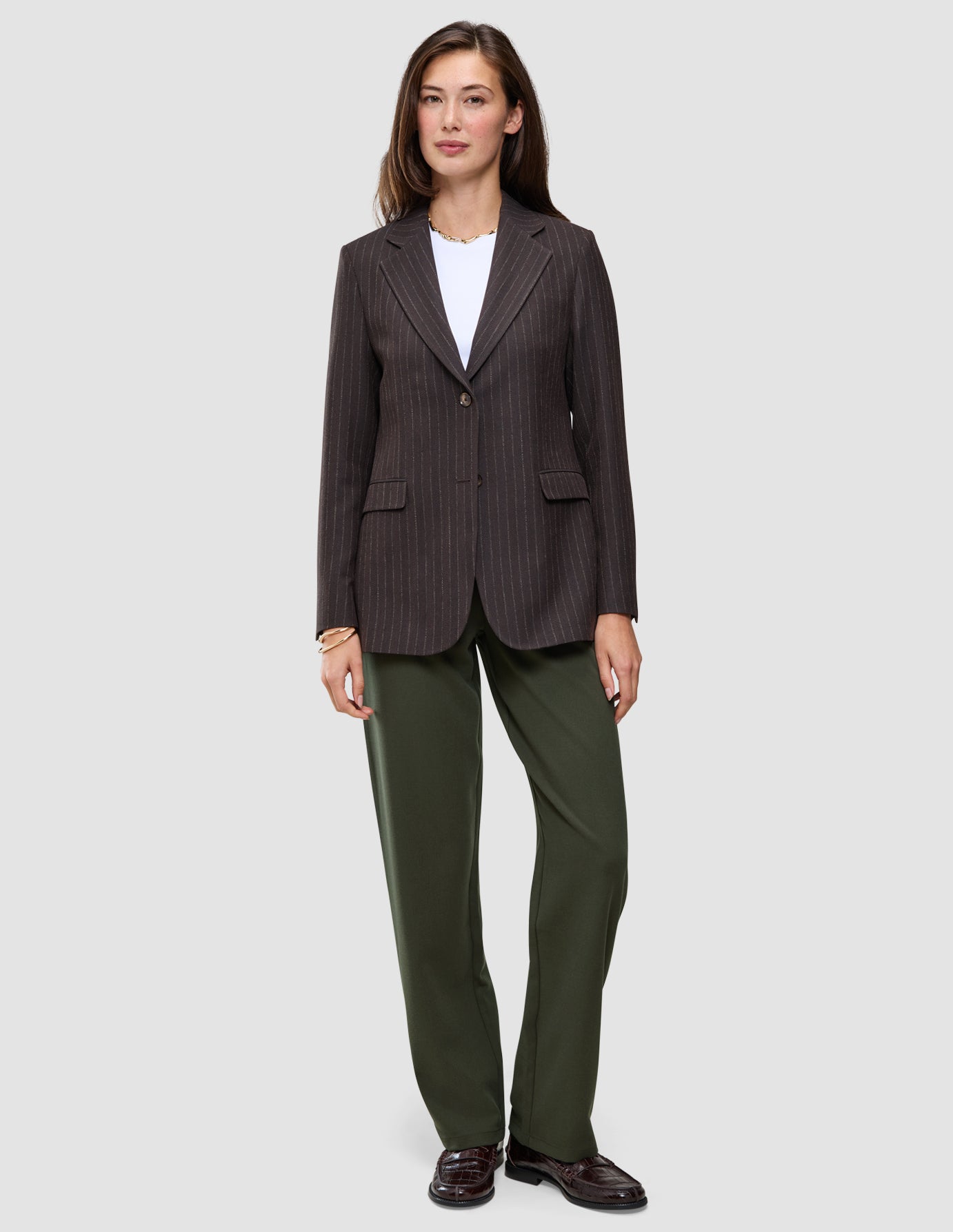 Eine Person trägt einen braunen Blazer mit Nadelstreifen über einem weißen T-Shirt, dazu die Hose Women GO2 Pants Straight Dusty Olive und dunkle Loafer – ein eleganter Look ganz im Sinne des skandinavischen Designs.